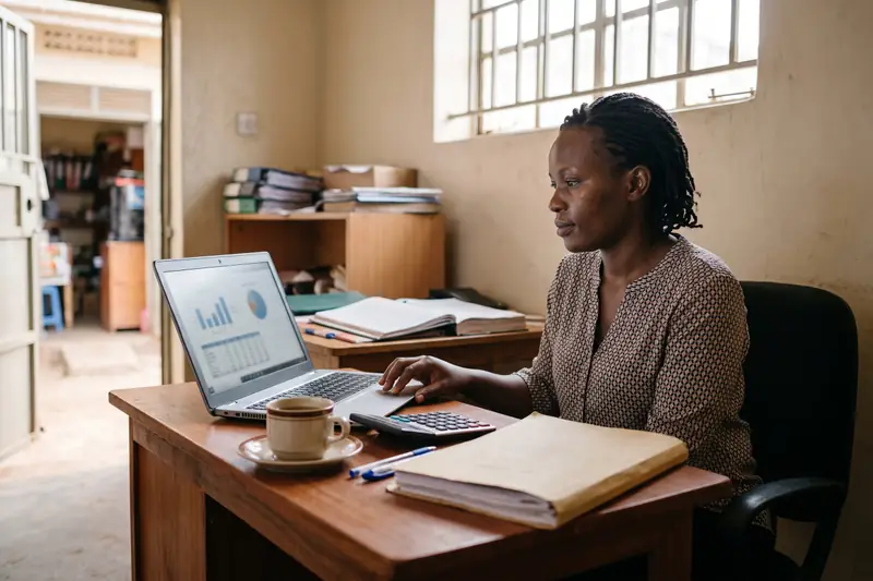 An accountant at her desk with a laptop showing charts, a calculator and a ledger